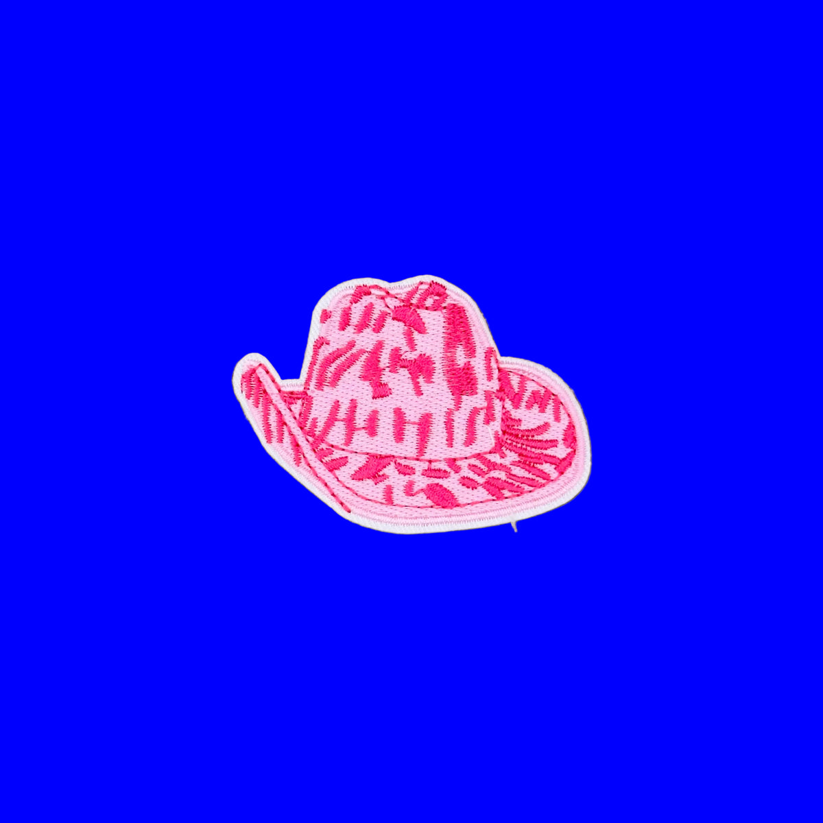 A small embroidered patch shaped like a cowboy hat, featuring a pink and white zebra-like pattern with a white border, placed on a solid brown background.