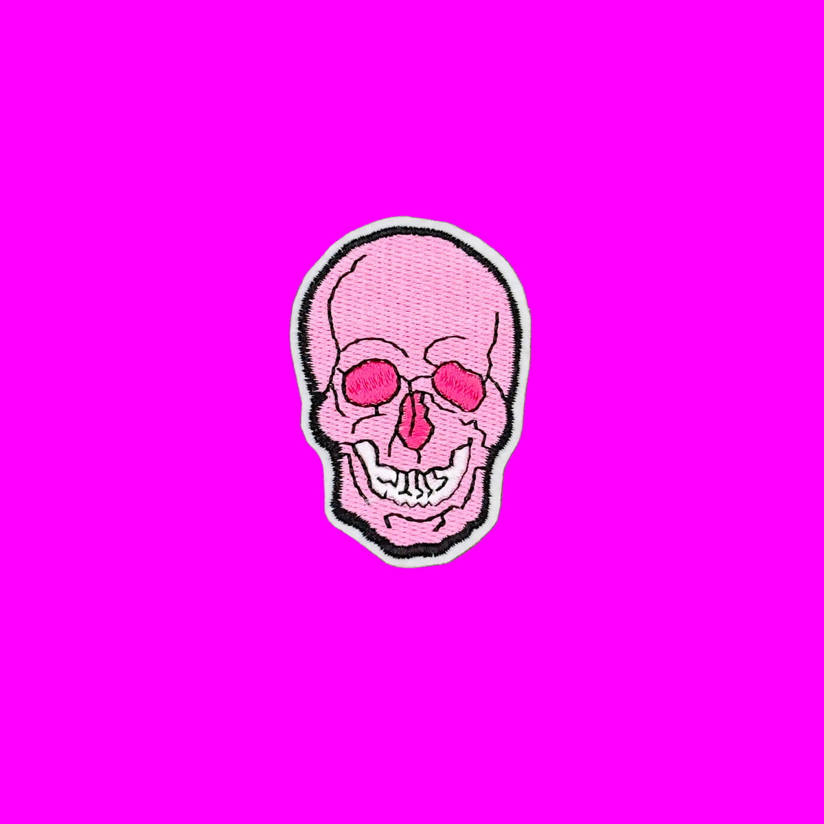 A pink embroidered skull patch with black and white outlines, placed on a solid brown background.