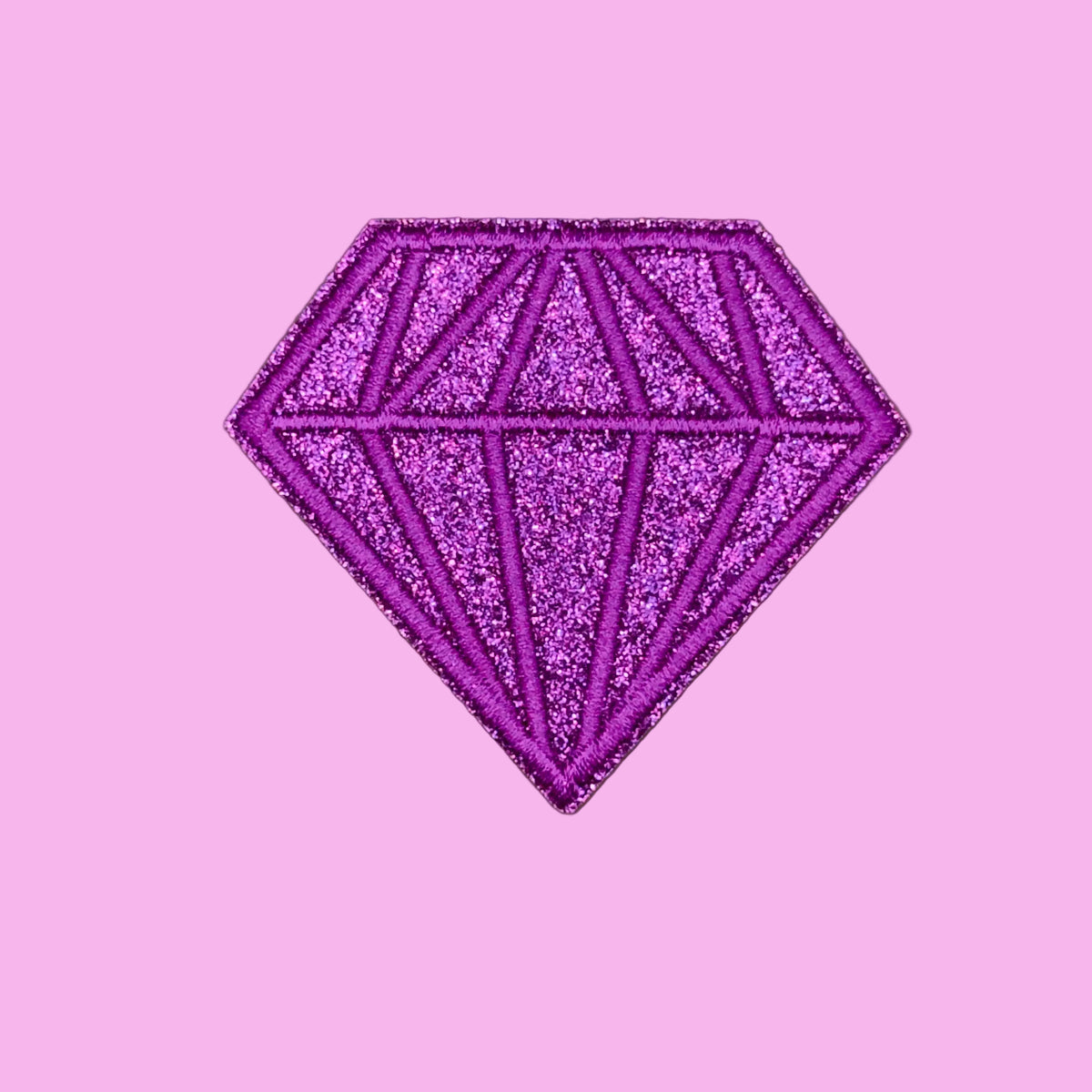A glittery purple diamond-shaped patch with a faceted gemstone design, shown on a solid brown background.