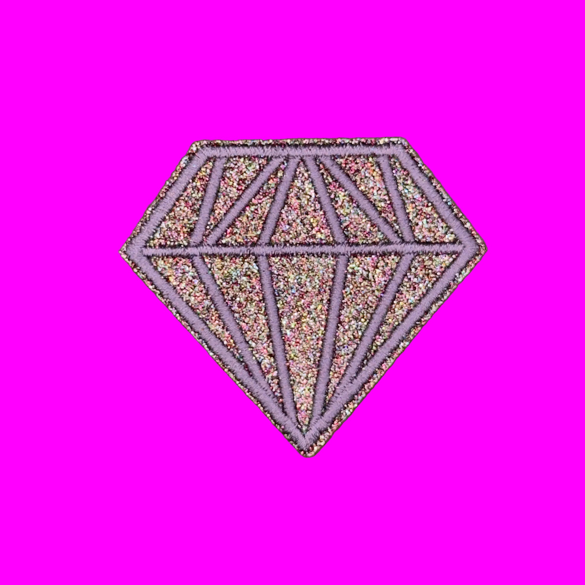A diamond-shaped glitter patch with a lavender purple outline and multicolor iridescent glitter fill, shown on a solid brown background.