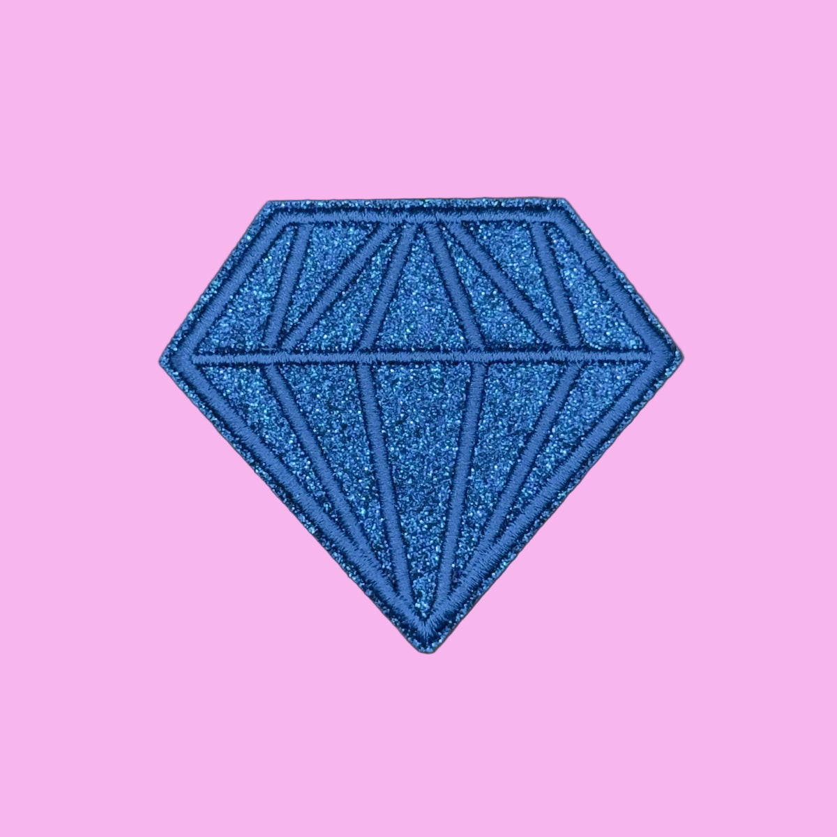 A blue glitter diamond-shaped patch with geometric line details, shown on a solid pink background.