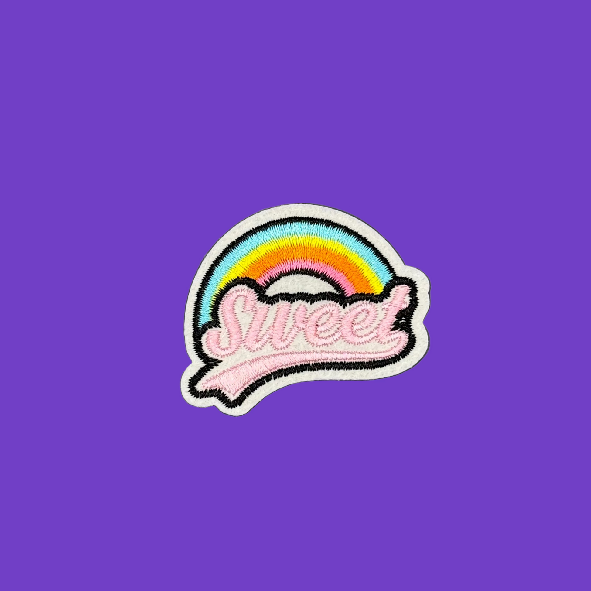 A colorful embroidered patch featuring a rainbow arch over the word 'Sweet' in pink script, placed on a solid purple background.