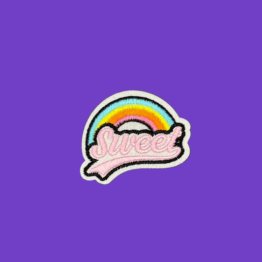 A colorful embroidered patch featuring a rainbow arch over the word 'Sweet' in pink script, placed on a solid purple background.