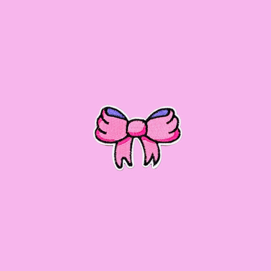 Small cartoon girly bow patch with pink and purple ribbon and a black outline embroidered iron on patch.