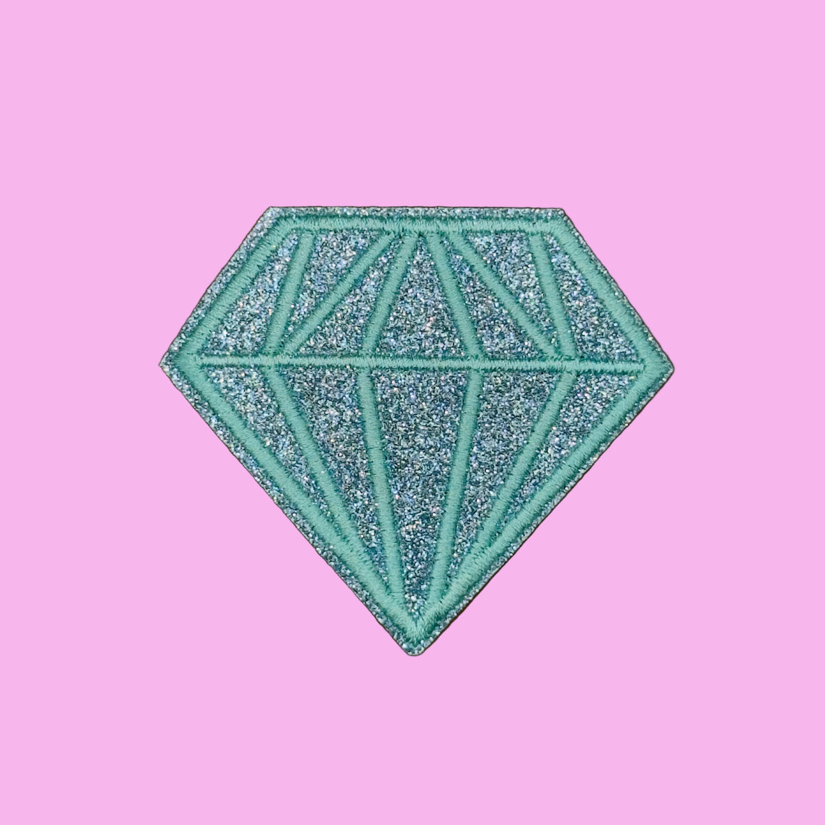 A glittery turquoise diamond-shaped patch with geometric line details, displayed on a solid brown background.