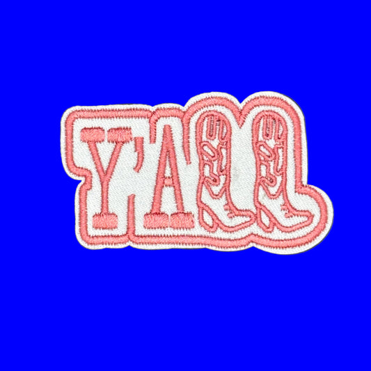An embroidered patch featuring the word 'Y'all' in coral pink letters with white outlines, set against a solid blue background.